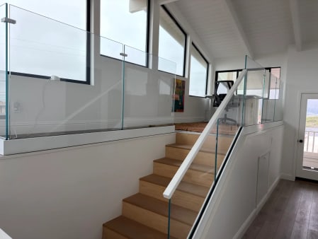 Continuous frameless glass wraps a loft edge and follows an oak stair below black-framed clerestory windows.