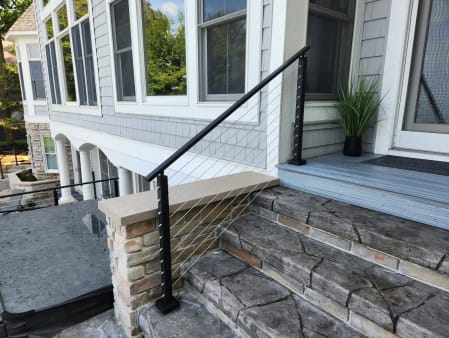 A black-post cable railing follows stone-veneer steps up to a gray-sided home.