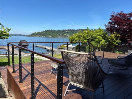 Black cable railing with a hardwood cap borders a rich hardwood deck with woven lounge chairs above a lake.