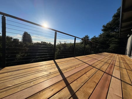 Wood-capped cable railing edges a wide new wood deck surrounded by treetops.