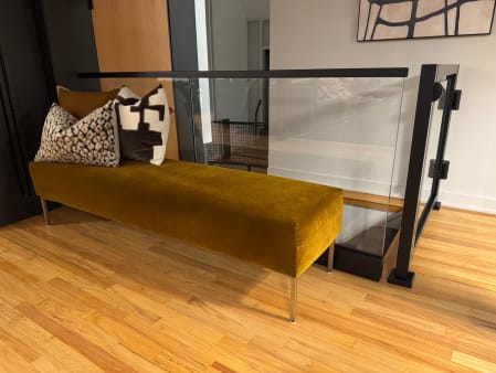 Black-framed glass railing and gate along a hardwood landing next to an upholstered bench.