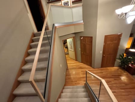 Frameless glass railing set in a base rail runs along a carpeted stair with a wood handrail in a traditional home.