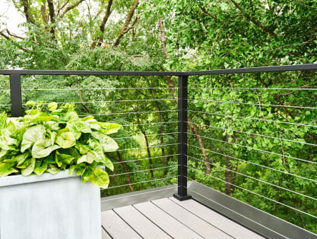 Black cable railing corner on a composite deck beside a concrete planter with leafy plants.