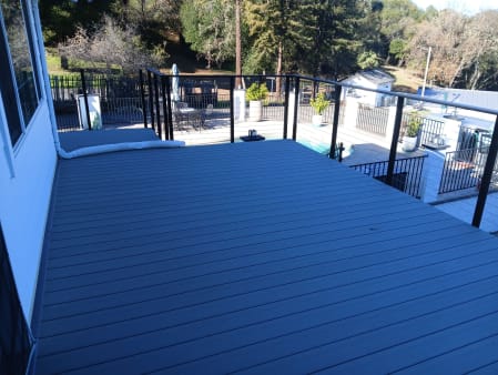 Black side-mount cable railing along a composite deck overlooking a backyard pool.