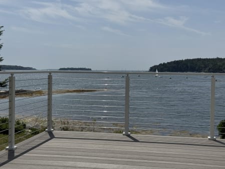 White cable railing frames a composite deck overlooking a calm bay with wooded islands.
