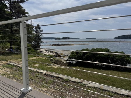 White cable post and rail with stainless cables looking out over a rocky shoreline and bay.