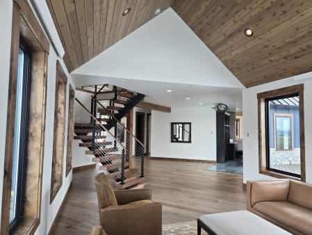 A black FLIGHT switchback with walnut treads and cable railing under a cedar ceiling in an open living room.