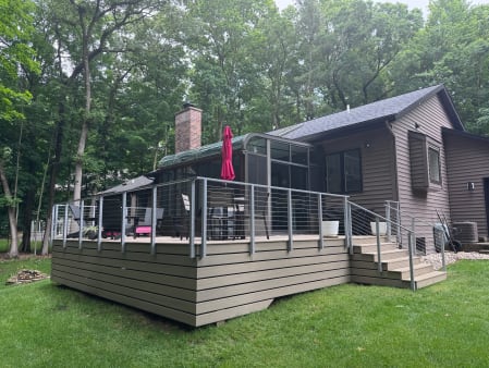 Wooded backyard composite deck and stair wrapped in gray-post cable railing beside a sunroom.