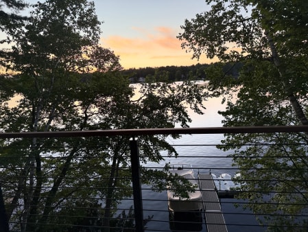 Jet black horizontal rod railing with a mocha hardwood handrail framing a lake and dock at sunset through the trees.