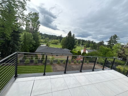 Large tiled balcony edged with black-post cable railing overlooking evergreen trees and a golf course.