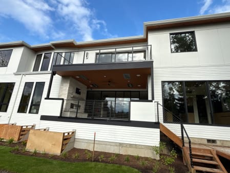 White modern home with black cable railing on the upper balcony, covered terrace and deck stair.
