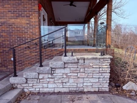 Black cable railing follows stacked limestone steps up to a brick home's covered porch.