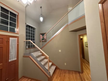Clear glass stair railing and frosted glass landing panels with oak cap rail in a two-story foyer.