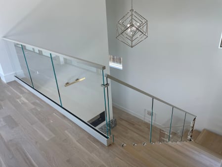 Frameless glass base rail railing with a slim handrail wraps a stair opening on white oak flooring.