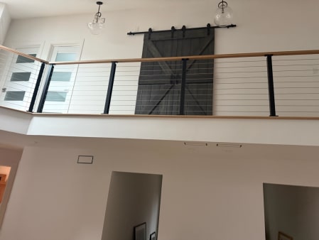Black-post cable railing with a white oak cap lines a loft with a barn door above a hallway.