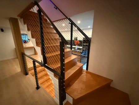 Black posts with cable infill and a black handrail follow a natural wood stair turning at a landing.