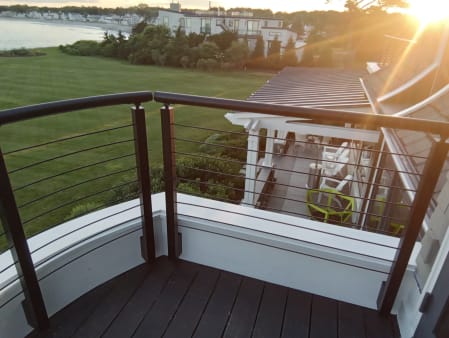 Bronze posts and rod infill with round handrail on a curved deck wall with sun flare over the coast.
