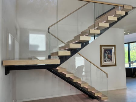 Light oak treads on a black mono stringer with frameless glass railing, wood handrail and LED lights.