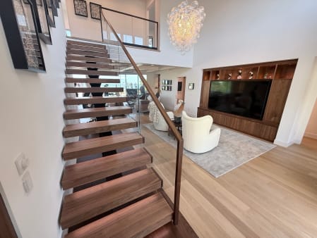 Walnut treads on a hidden mono stringer with frameless glass railing and wood handrail rising into a bright living room.