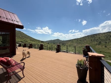 Wide composite deck edged by black cable railing and wood posts, looking out over a mountain valley.