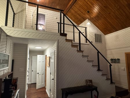 Black cable railing runs up a cabin staircase and around the loft beneath a vaulted pine ceiling.