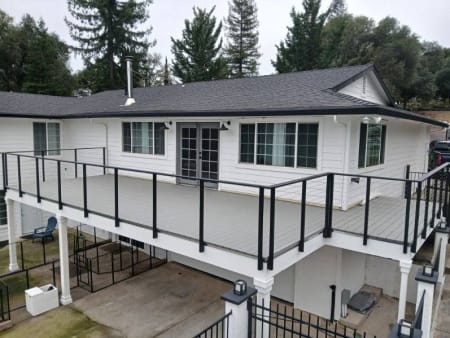 Black posts with cable infill run along a long raised deck on a white ranch home.