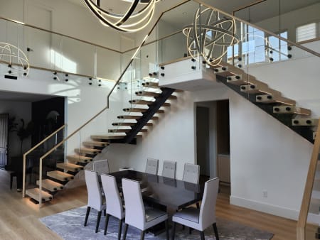 Black-stringer FLIGHT Mono stairs with oak treads and standoff-pin glass railing overlook a formal dining room.