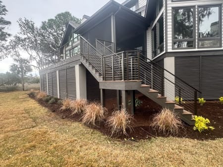 Horizontal rod railing follows an exterior stair and wraps a raised deck above landscaped beds.