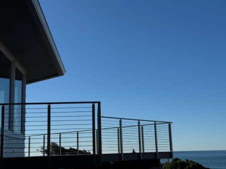 Stainless cable railing wraps a raised deck silhouetted against a clear blue sky above the ocean.