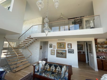 Floating wood stair rises along a stone wall to a loft with frameless glass railing and wood cap.
