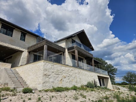 Frameless glass on talon spigots lines two terraces of a limestone hill-country home