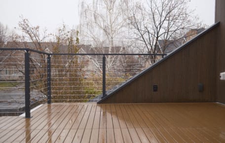 Black cable railing on a composite deck changes height beside an angled wood-clad wall.