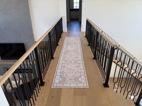 Black decorative iron baluster railing with oak handrails lines an upstairs bridge with a runner rug