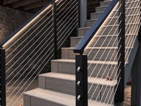 Close view of black posts, stainless cable and an LED-lit handrail along a composite deck stair.
