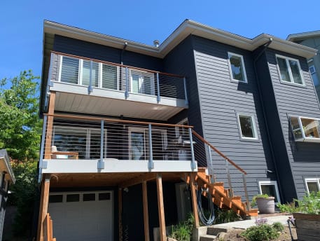 Stainless cable railing lines stacked balconies and an exterior stair on a dark-sided home.