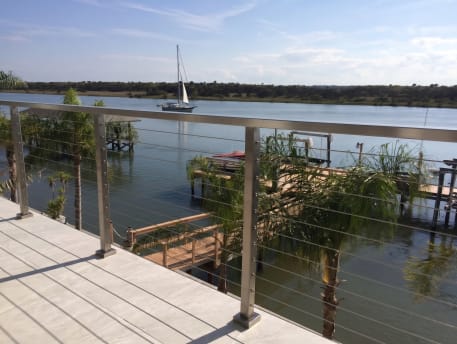 Stainless cable railing on a light tile balcony overlooking a dock, palms and a sailboat on the water.