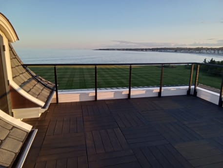 Bronze posts with horizontal rod infill and round handrail around a rooftop deck overlooking the ocean.
