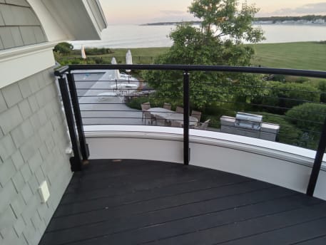 Bronze rod railing with round handrail following a curved balcony wall above a seaside lawn.