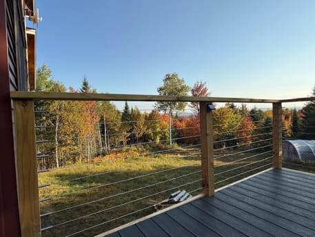 Cable infill between wood posts and cap rail along a composite deck overlooking autumn woods.