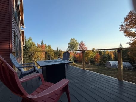 Wood-post cable railing around a dark composite deck with Adirondack chairs and fall foliage.
