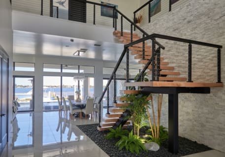 Wood floating treads on a black mono stringer with a support column and cable railing rise over an indoor planted rock garden.