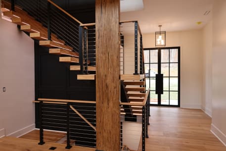 Ash floating switchback stair with black cable railing around a timber column in a bright entry