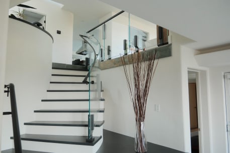 Black talon-clamped glass panels curve along a white stair with dark treads in a bright modern entry.