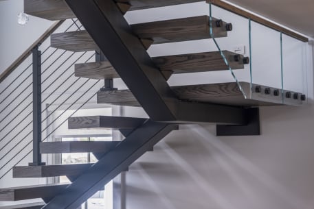 Rift oak treads on a black mono stringer with glass on standoff pins and cable railing beyond.
