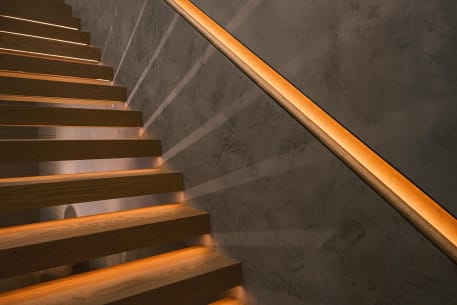 A recessed LED-lit leather handrail runs along a plaster wall above floating oak treads with warm under-lighting.