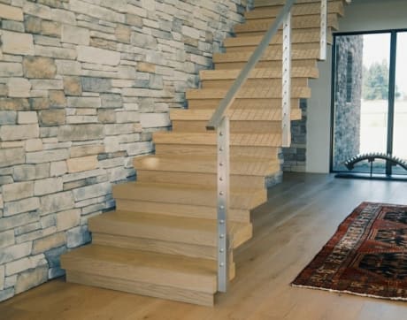 White oak stack stair with stainless cable posts rises along a stacked stone wall.