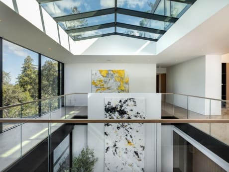 Glass railing with a white oak cap rail encircles an open atrium beneath a large skylight with forest views.