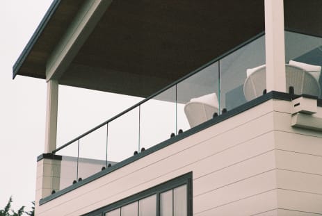 Frameless glass on black talons with a black top cap along a covered balcony on a white-sided home.