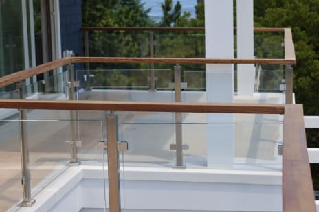 Glass panels in stainless posts with a hardwood top rail wrap a coastal balcony near the water.