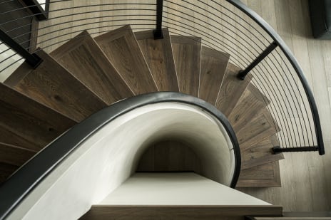 Overhead view of a spiraling wood-tread stair wrapped by black curved rod railing.